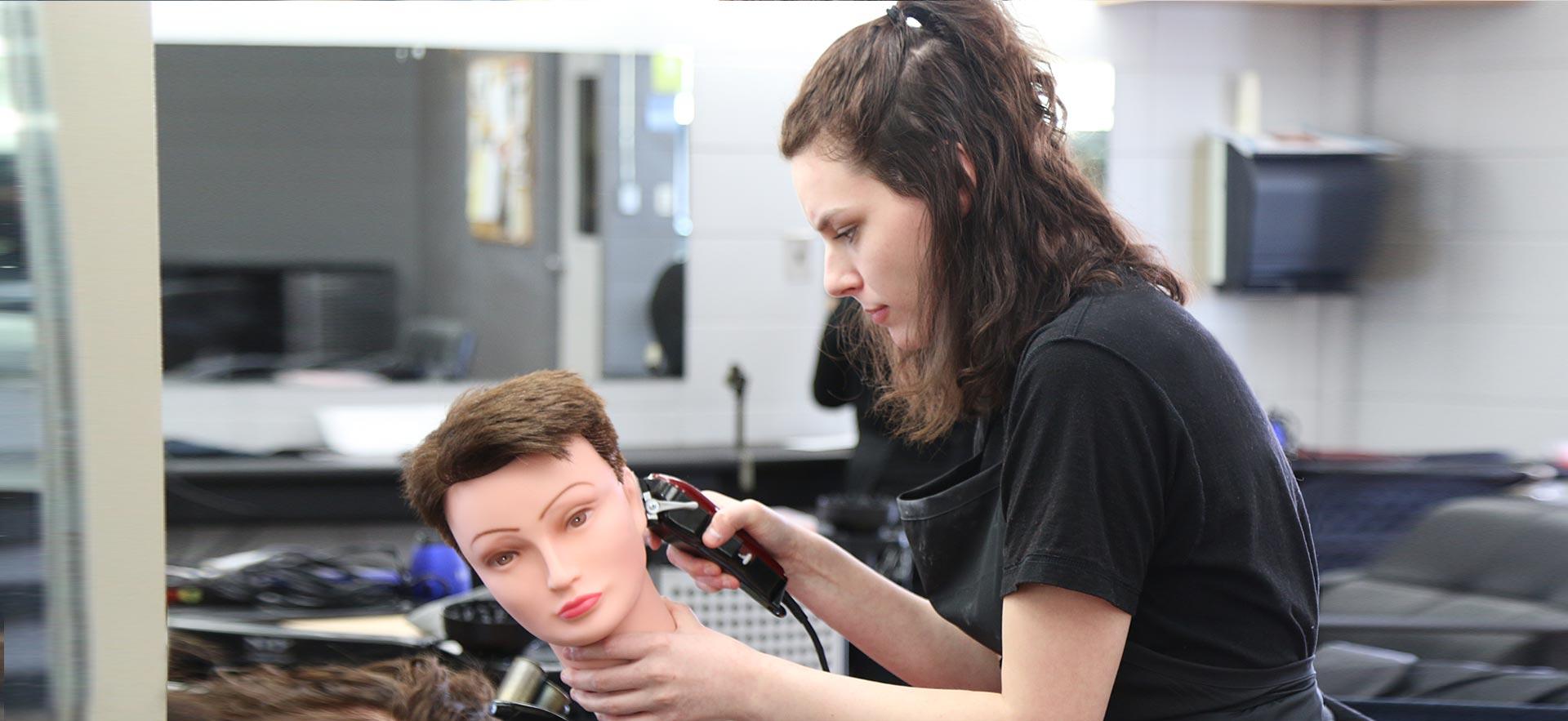 One female hairstylist student cuts the hair of a mannequin in class.