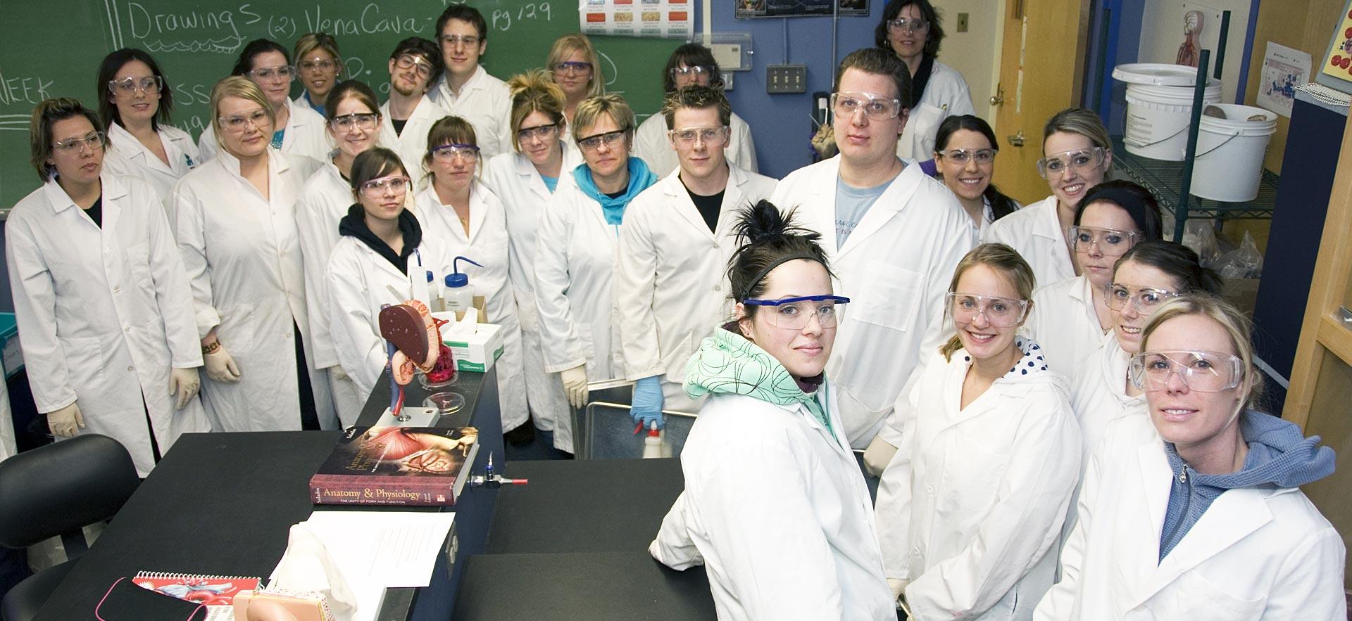 Nursing class in lab coats smile for photo.