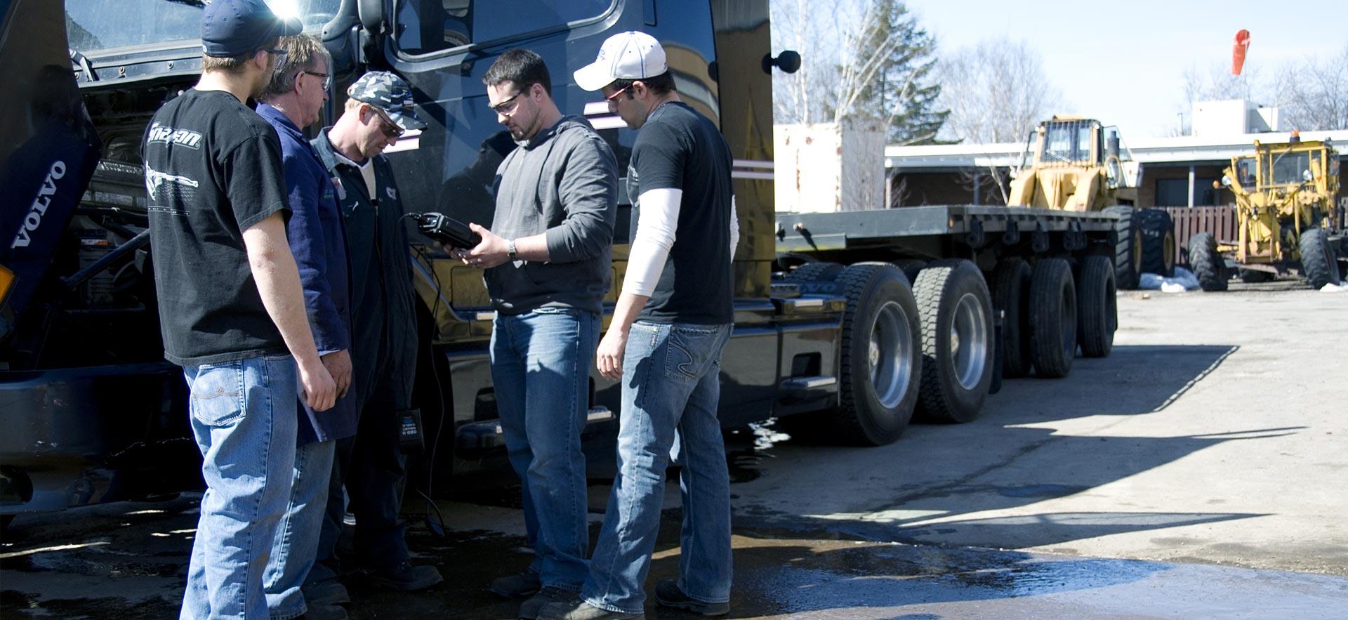 A group of male heavy equipment students discuss repairs on a truck.