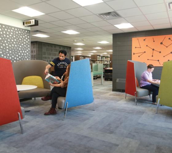 seating area in newly renovated library showing two students looking at a book together and one using their laptop
