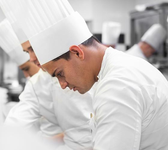 Josh Adamo graduate shown in chef uniform in kitchen