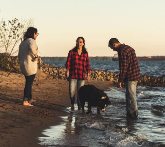 Three people standing with a dog on the shore of a beach 