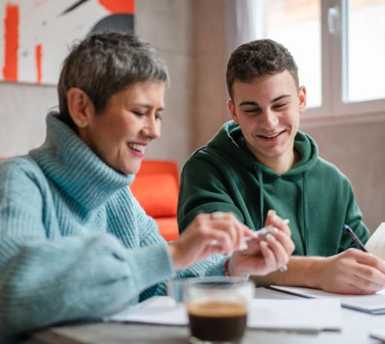 Adult woman sitting beside student at a desk smiling and looking down at papers