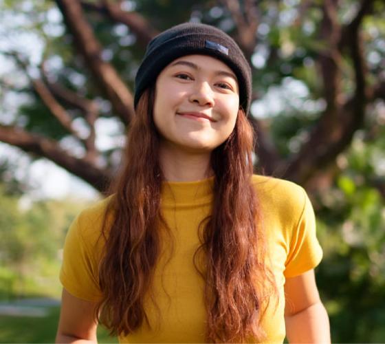 Student smiling at the camera outside with green grass and tree behind her