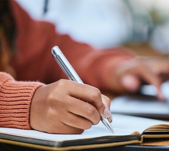 Student's arms shown with pen in hand writing in a notebook