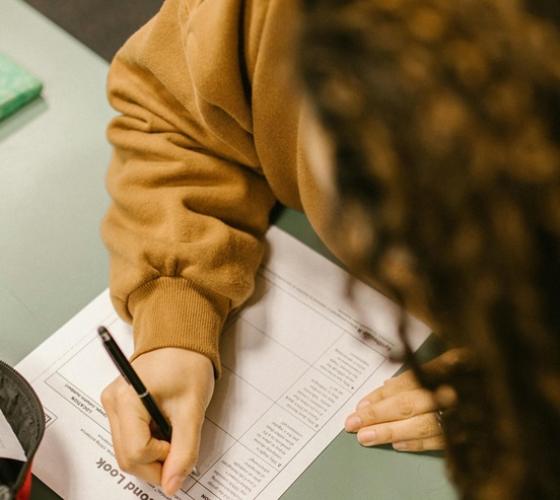 Student at desk looking down at paper with pen in hand writing