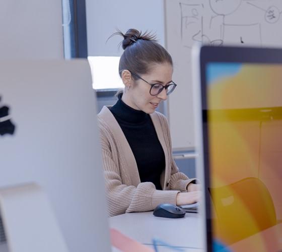 Graphic design student working in the Mac lab with computers visible