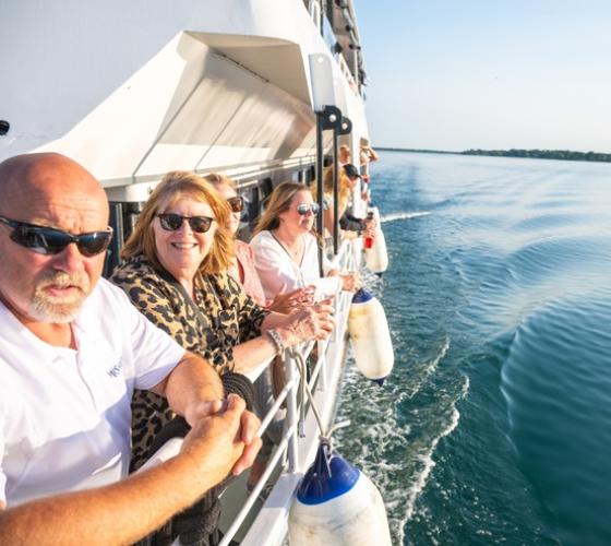People smiling at camera on deck of Miss Marie boat on water