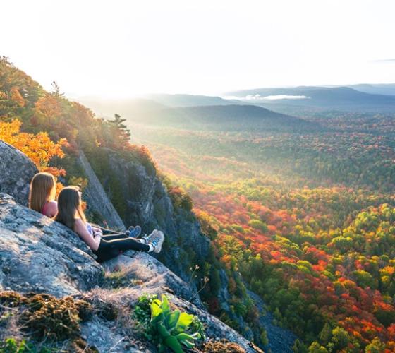 Two women sitting on cliff ledge on Robertson Cliff overlooking fall colours