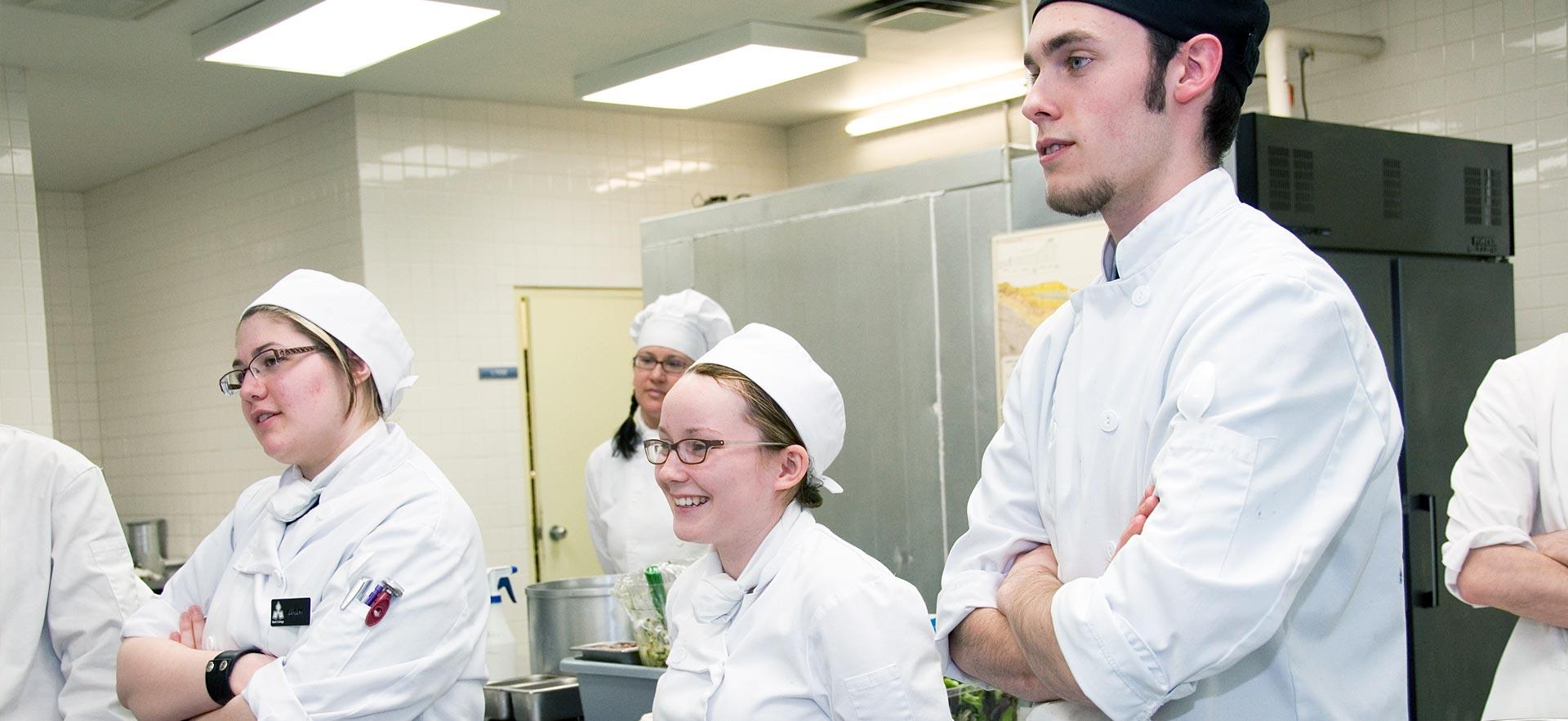 A group of culinary students listen to their instructor in one the Sault College culinary kitchens.