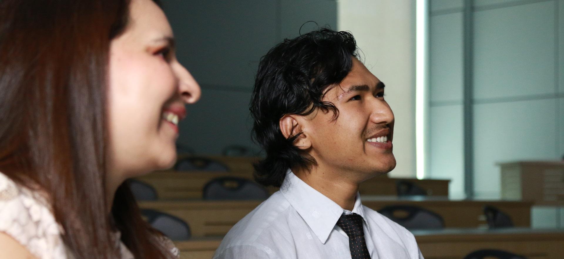 Two business students in class smiling looking towards instructor off screen
