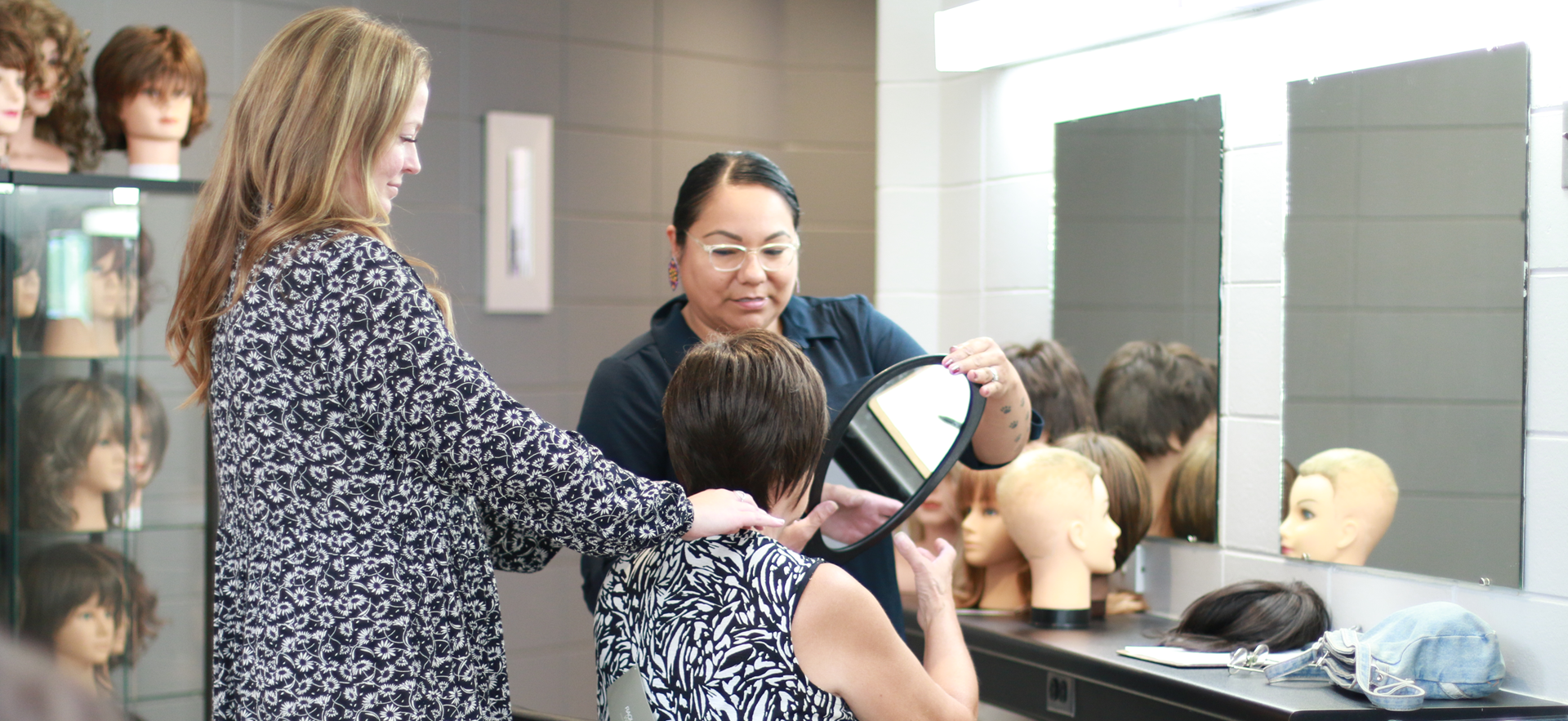 Hairstyling student and instructor helping client during a wig fitting