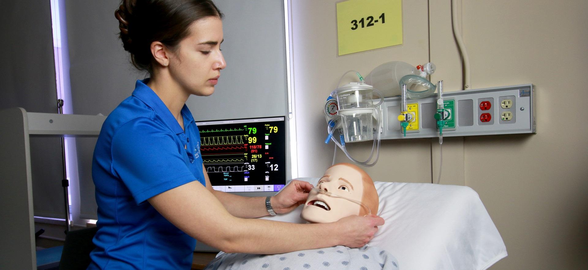 Nursing student adjusting oxygen line under nose of simulation manikin