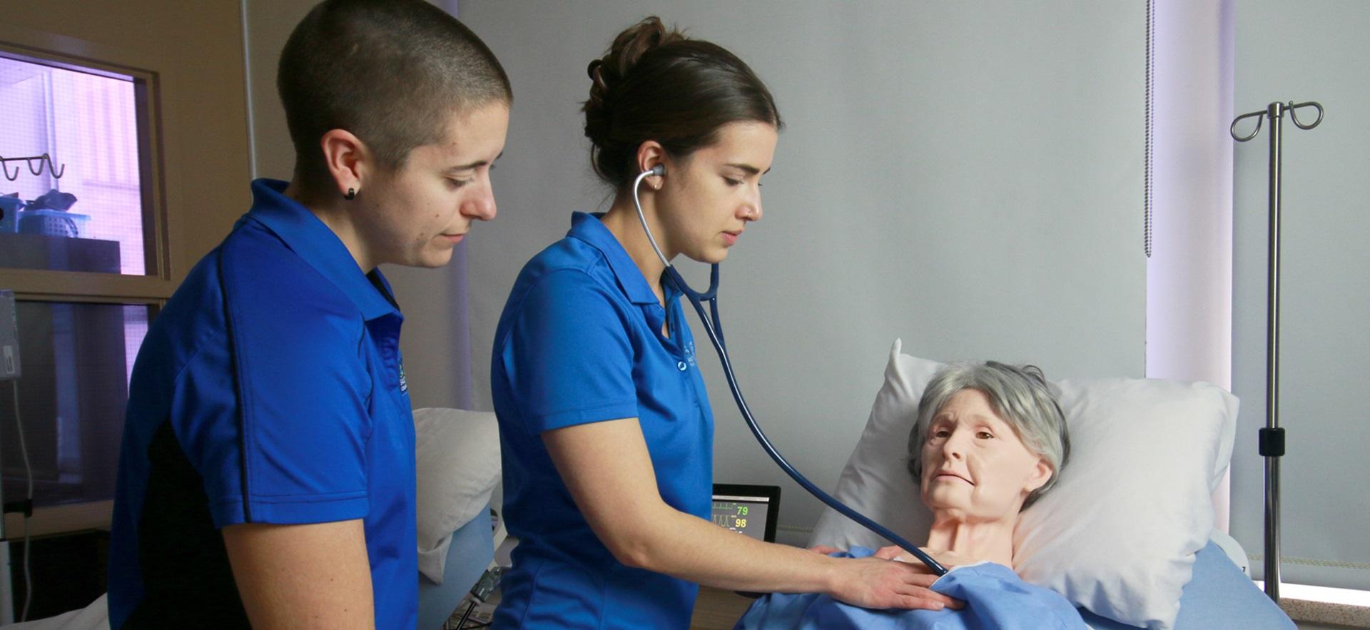 Nursing students with an elderly sim manikin checking vitals