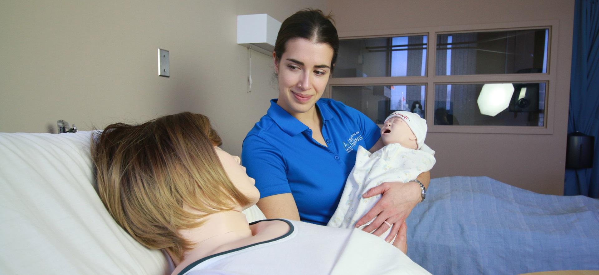 Nursing student holding infant sim manikin and at the bedside of the mother sim manikin