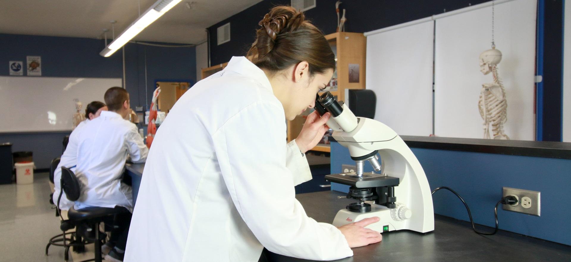 Nursing student in the lab looking through a microscope with students in background