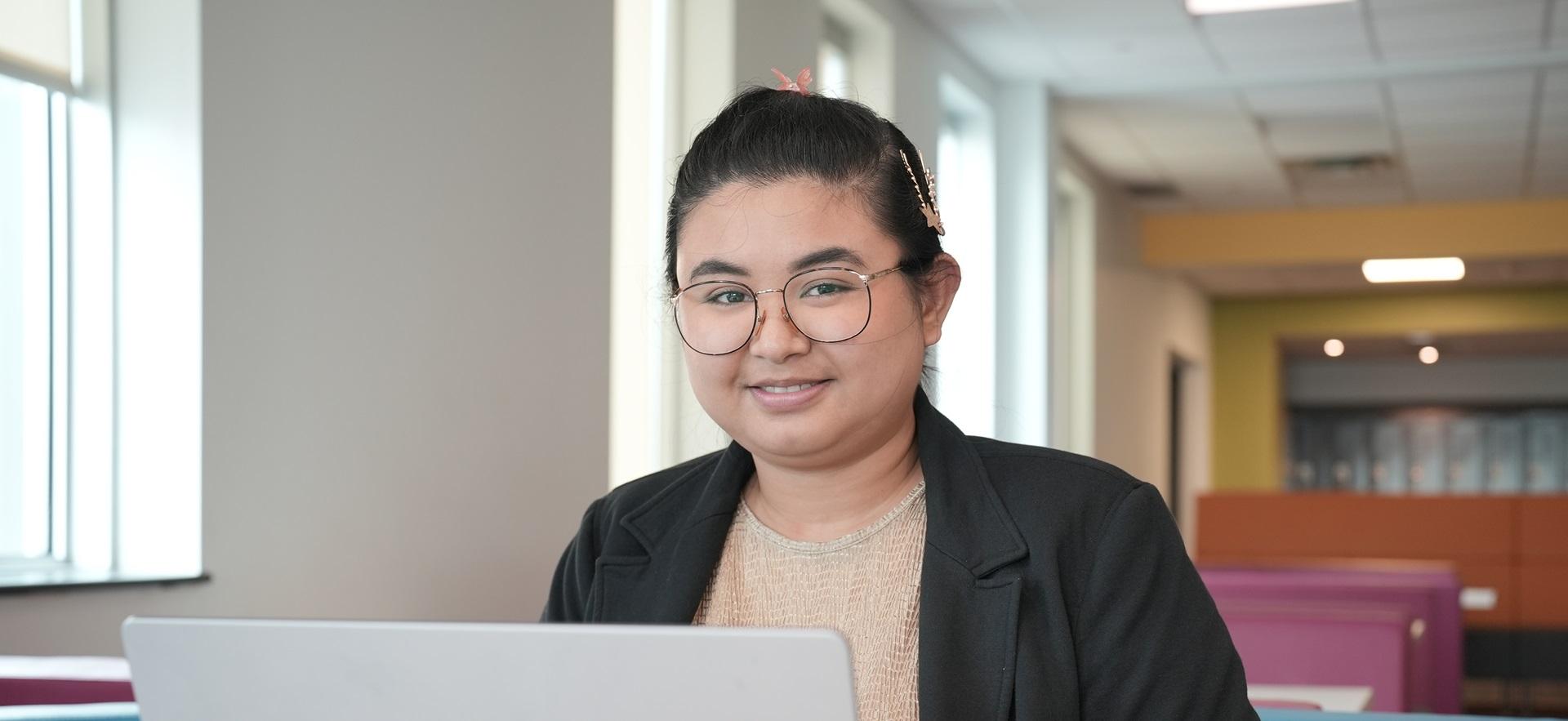 Student working on laptop in common area smiling at camera