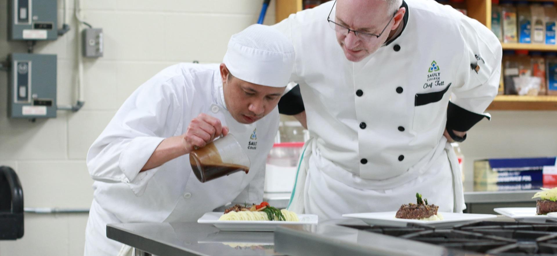 Culinary student prepping a dish with instructor onlooking