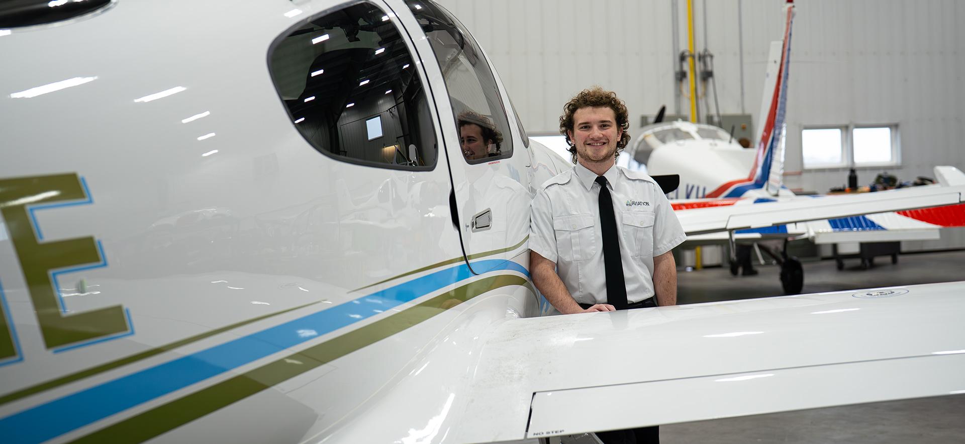 Aviation student smiling at camera leaning on Cirrus aircraft