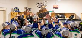 Women's hockey team gathered together in changeroom holding up trophies